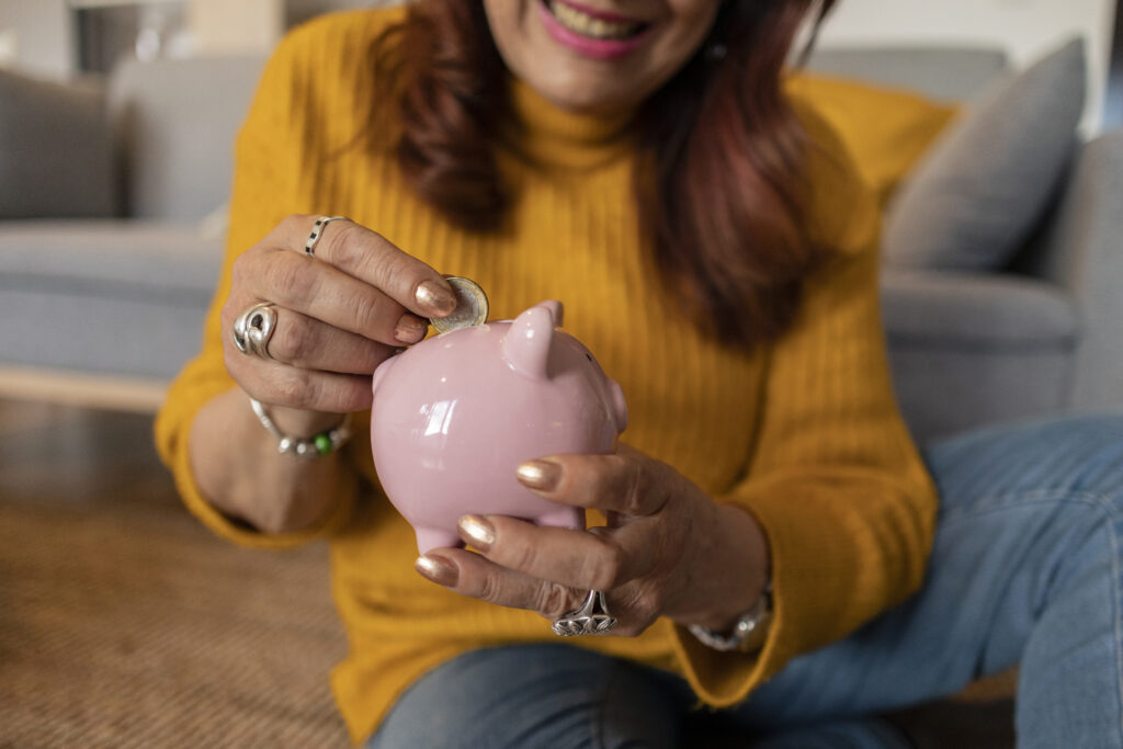 Saving mature woman puts a coin in piggy bank